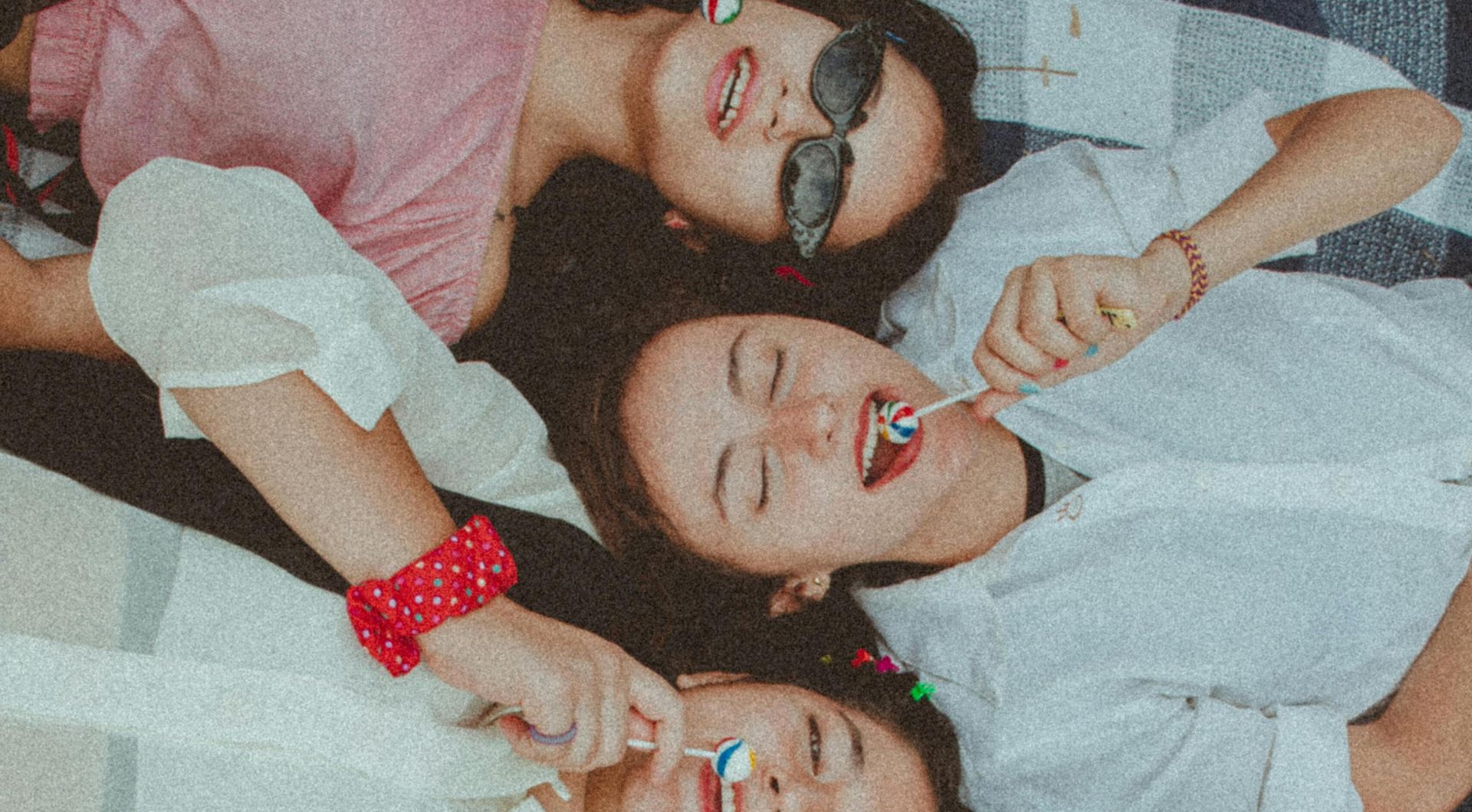 Joyful group of diverse women enjoying a sunny picnic with lollipops, showcasing friendship and fun.