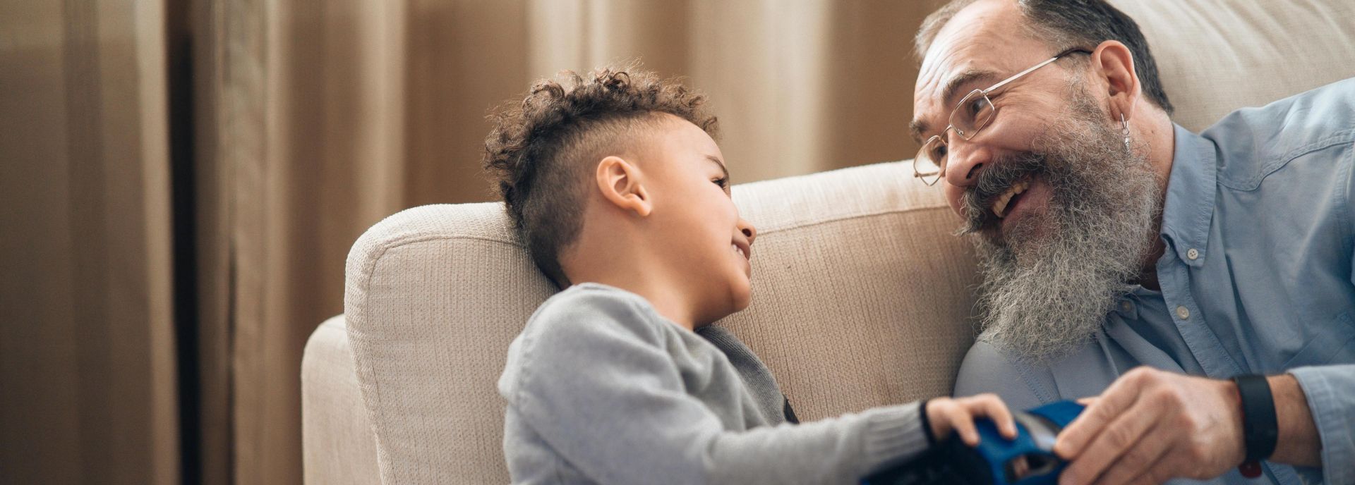 A joyful grandfather and grandson sharing a playful moment on the couch, indoors.